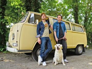 Zwei Männer mit Hund vor einem alten VW-Bus